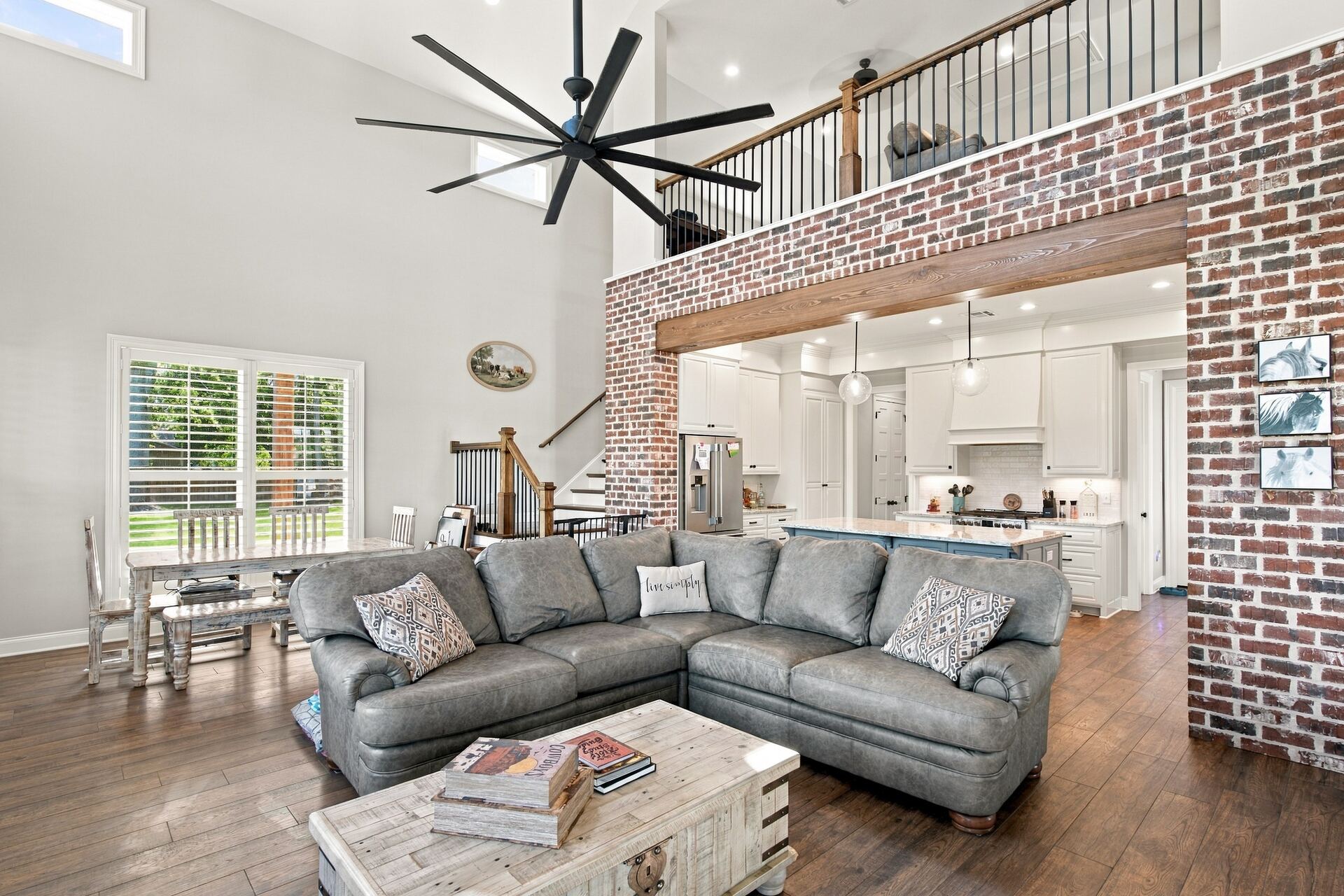 Two-story great room with exposed brick, black ceiling fan and open kitchen
